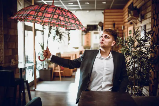 Photo of Sad Male Sitting Alone In Coffee Bar And Opening Umbrella