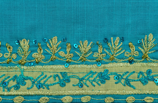 Beautiful artful embroidery with gold threads with rhinestones and sequins on a calico blue fabric. Traditional Indian pattern on saree robe