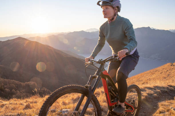 istock Female mountain biker rides up grassy mountain ridge at sunrise 1301828821