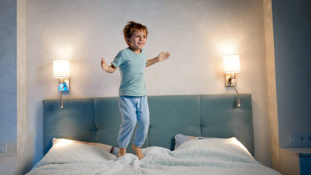 glad skrattande och leende småbarnspojke i pyjamas hoppar och hoppar högt upp på förälderns säng på natten innan han somnar - happy slowmotion bildbanksfoton och bilder