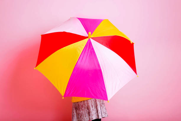 istock Girl is hiding under a colored umbrella on a pink background. 1301832293