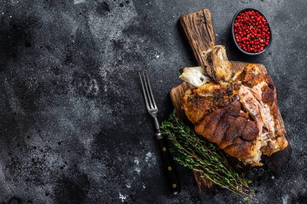 istock Roasted pork knuckle eisbein on a wooden board with herbs. Black background. Top view. Copy space 1301835567