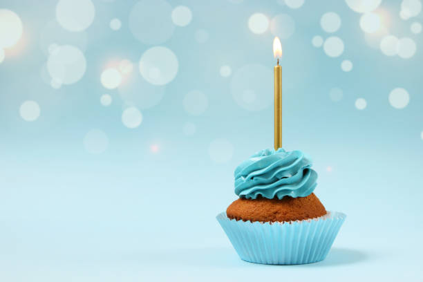 cupcake with cream and a burning candle for a birthday or other holiday with a shopping plan on a colored background with bokeh lights - cupcake birthday birthday cake first place imagens e fotografias de stock