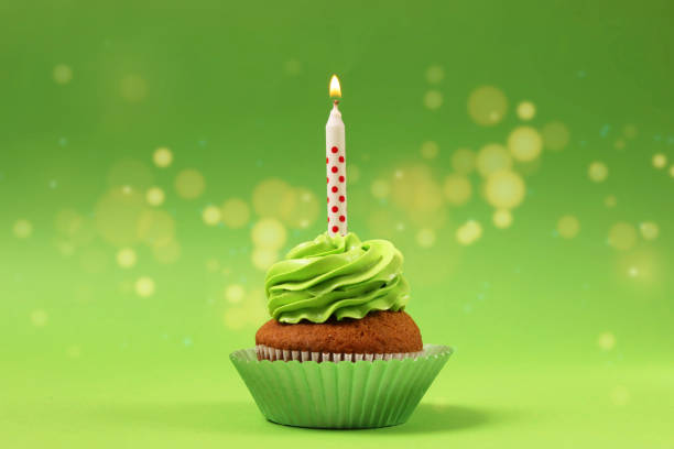 cupcake with cream and a burning candle for a birthday or other holiday with a shopping plan on a colored background with bokeh lights - cupcake birthday birthday cake first place imagens e fotografias de stock