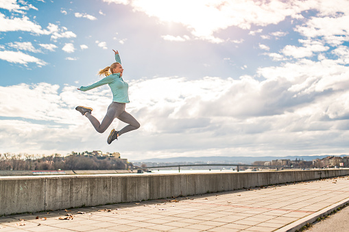 Healthy mid adult woman running in the city and jumping on a beautiful sunny winter day.