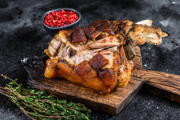 istock Roasted pork knuckle eisbein on a wooden board with herbs. Black background. Top view 1301838377