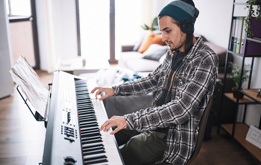 Young artist with an electric piano and headphones creating new music at living room.