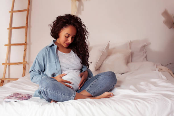 joven mujer afroamericana bastante embarazada acostada en la cama, concepto de personas de estilo de vida - abdomen fotos fotografías e imágenes de stock