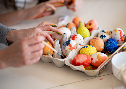 Hands painting on eggs. In egg carton are boiled eggs in different colors, drying. There are yellow, red, blue, orange, spotted and multi-colored eggs. Close up.