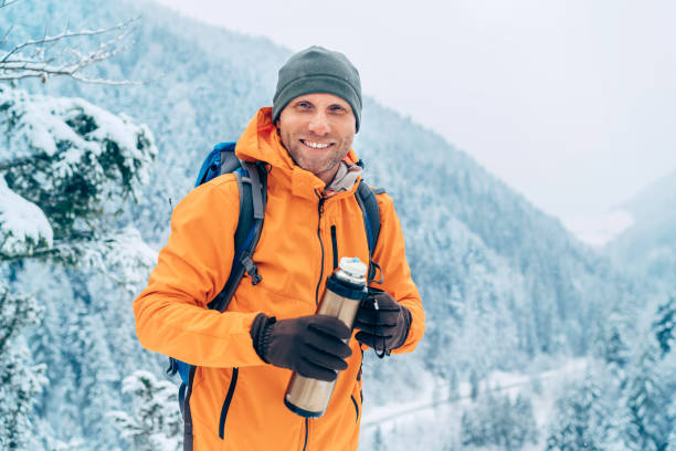 istock Laughing Man dressed bright orange softshell jacket with a hot drink thermos flask looking at camera while he trekking winter mountains route. Active people in the nature concept image. 1301848230