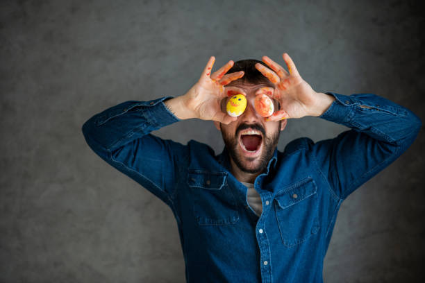istock Happy man in denim shirt is playing with Easter eggs, making silly faces. 1301853637