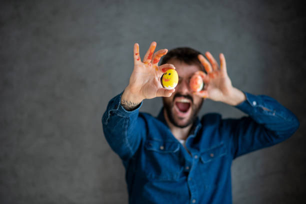 Young man is holding orange and yellow Easter eggs. He was painting on boiled eggs with his family in various colors using paintbrushes and tempera colors.