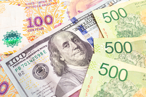 Argentine pesos and US dollar. Money, cash, exchange. Group of Argentine pesos banknotes with a 100 US dollar bill in close-up. Photograph representing the exchange between ARS and US DOLLAR.