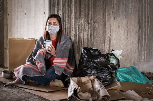 Asian woman homeless wearing hygiene face mask for protective infection and pandemic of coronavirus or covid19. Asian woman homeless wearing hygiene face mask for protective infection and pandemic of coronavirus or covid19. Female beggar wearing sweater and blanket sitting hold bowl for help on walkway street homeless person stock pictures, royalty-free photos & images