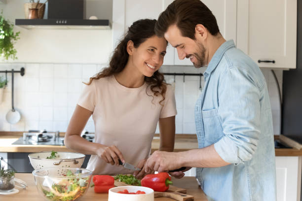 jeunes conjoints positifs faisant cuire la nourriture appréciant la conversation plaisante à la cuisine - bon appetite photos et images de collection