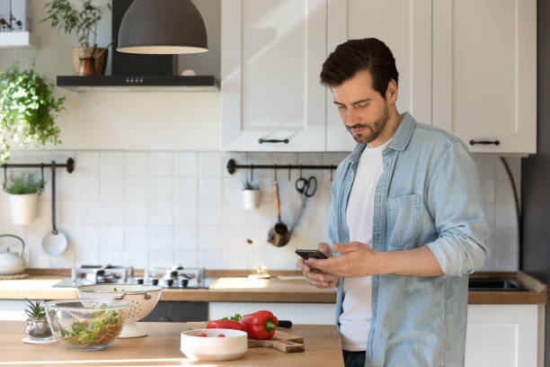 Millennial male preparing food holding smartphone ordering missing ingredients online