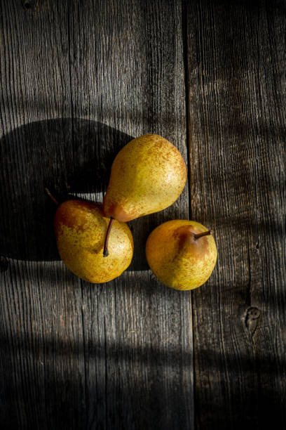 istock Three yellow pears on a barn wood plank table with shadows from the sun 1301871646