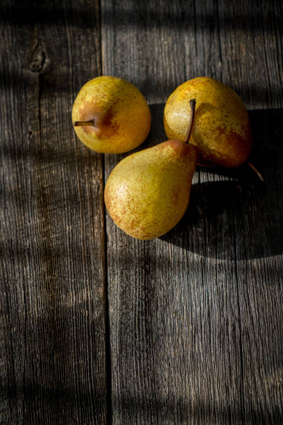 istock Three yellow pears on a barn wood plank table with shadows from the sun 1301872042