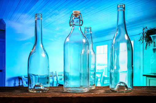 Four transparent glass bottles on a barn wood table in front of a blue background