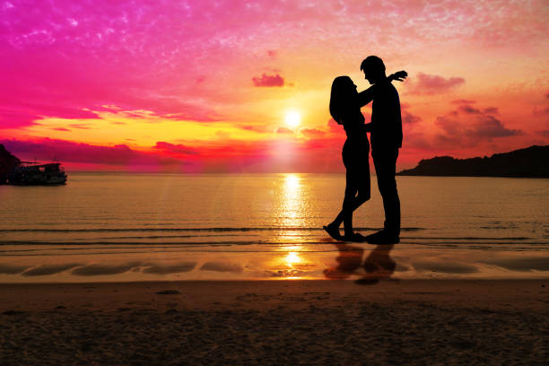 Silhouette happy young couple embracing each other with sunset at tropical beach with copy space. People standing on the beach with beautiful sky. Concept love and valentines day.