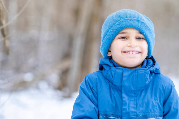 7 year old boy smiling at the camera while on a walk through a snowy forest on a chilly day.
