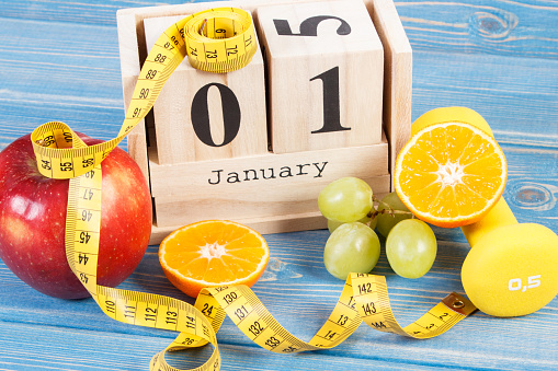 January 1 on cube calendar, fresh ripe fruits, dumbbells and tape measure, new years resolutions of healthy lifestyle