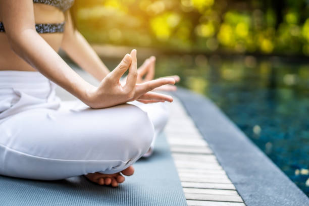 vista ravvicinata delle mani e delle gambe incrociate in posizione di loto, pratica yoga e meditazione femminile in posizione yoga al loto nella piscina blu - water lily swimming pool health spa water foto e immagini stock