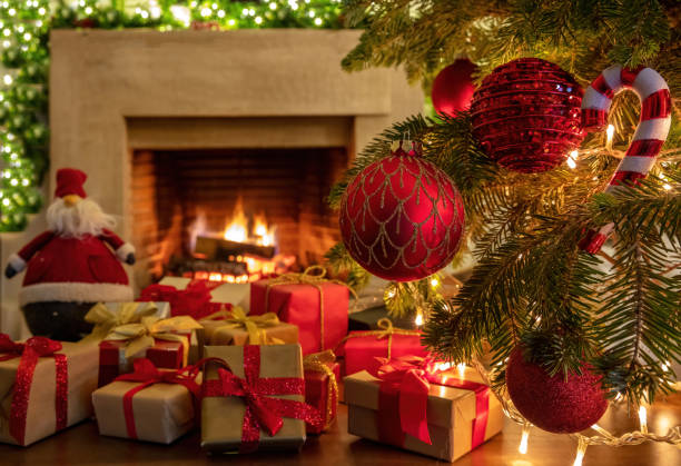 istock Xmas tree branch with red balls, gift boxes, blur burning fireplace background. 1301895547