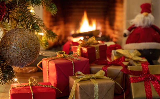 istock Xmas tree branch with silver golden ball, gift boxes, blur burning fireplace background. 1301895551