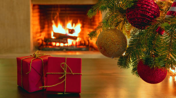 istock Xmas tree branch with balls, red gift boxes, blur burning fireplace background. 1301895557
