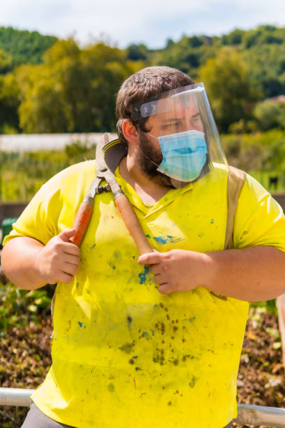 istock Worker in a recycling factory or clean point and garbage with a face mask and plastic protective screen, new normal, coronavirus pandemic, covid-19. Portrait with reflective vest and giant scissors 1301896337