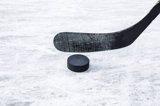 istock Black hockey stick and rubber puck on ice background. Closeup. Front view. 1301904852