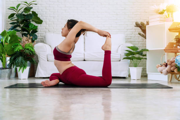 istock Activity young women sitting on mat in front of white sofa while doing position yoga eka pada rajakapotasana in living room. Relaxation girl practice advanced yoga at home. Lifestyle healthy concept. 1301909589