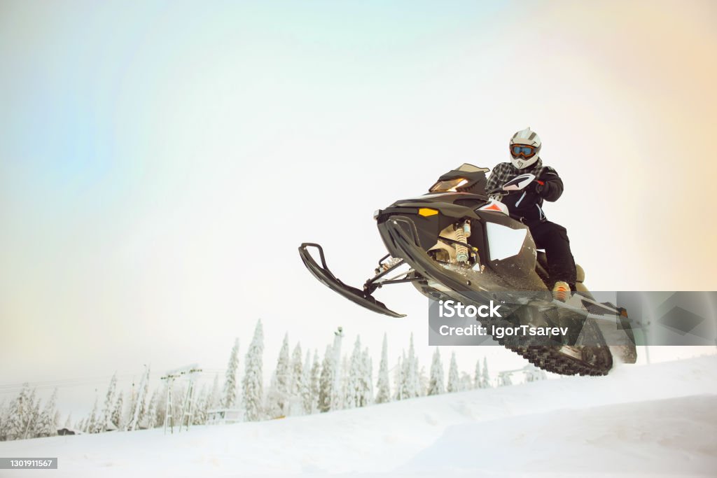 The rider in gear with a helmet making flying jumping taking off on a snowmobile on a background of a winter scenic landscape with mounting and sky. The rider in gear with a helmet making flying jumping taking off on a snowmobile on a background of a winter scenic landscape with mounting hillside and sky. Snowmobile Stock Photo