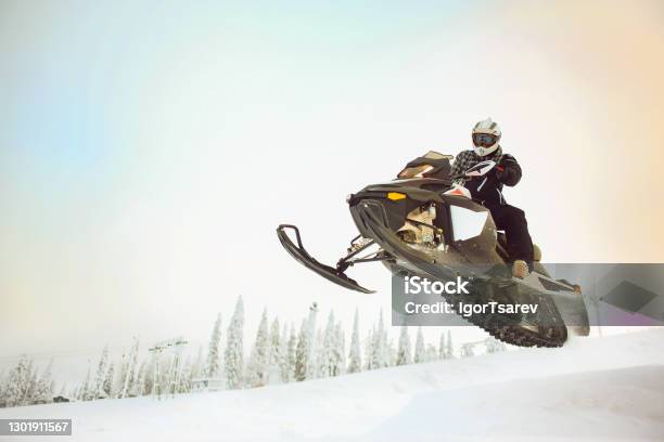 The Rider In Gear With A Helmet Making Flying Jumping Taking Off On A Snowmobile On A Background Of A Winter Scenic Landscape With Mounting And Sky Stock Photo - Download Image Now