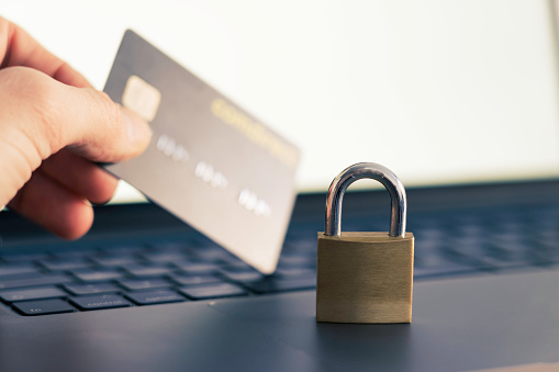 Image illustrating the concept of security and encryption while online shopping, banking and investing. There is a hand holding a credit card next to a laptop with a lock in the foreground.