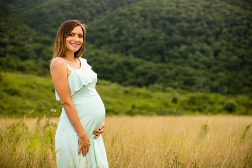 Pretty young pregnant woman relaxing outside in nature at summer day