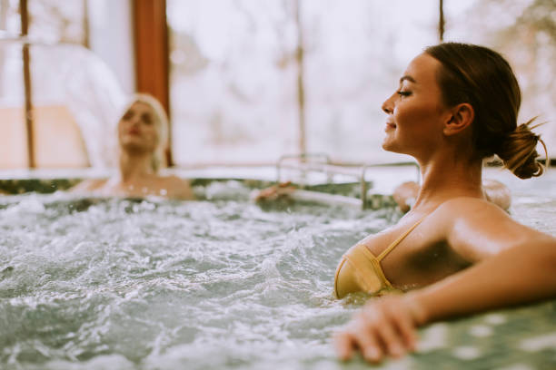 jeunes femmes détendant dans la baignoire de bain à remous au bord de la piscine - health spa swimming pool relaxation indoors photos et images de collection