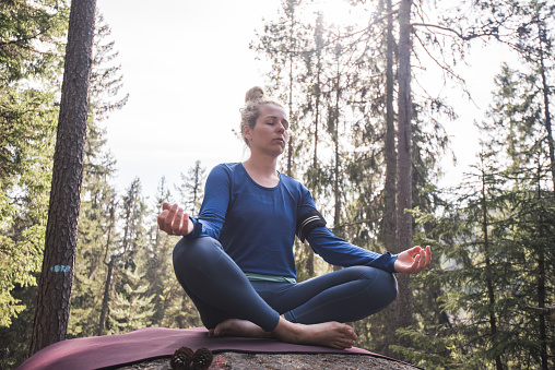 Young female doing yoga in evergreen forest.