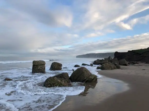 Beach at Reighton Gap under clouded sky with light breaking through Mist and Sea Fret with the surf breaking against the post war sea defences, sky reflects in rock pools, East Riding, Yorkshire Coastline, Yorkshire, England, United Kingdom
