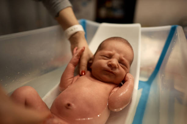 istock Small baby first bathing on mother hands, bathing in small plastic bath 1301931130