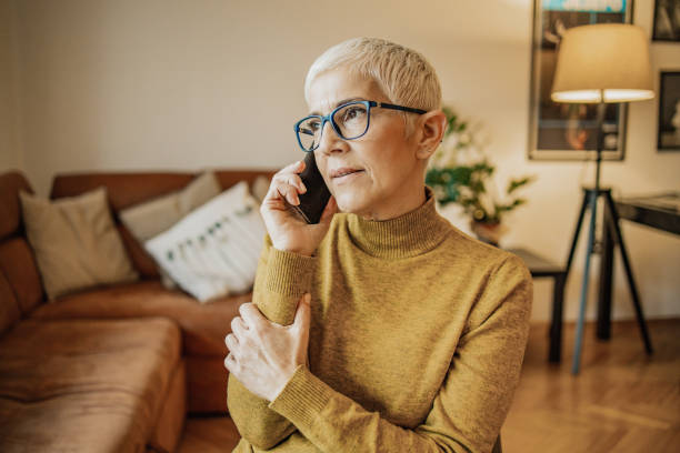 Beautiful senior woman is talking on the phone in the living room A worried senior woman with short gray hair is talking on the phone using phone stock pictures, royalty-free photos & images