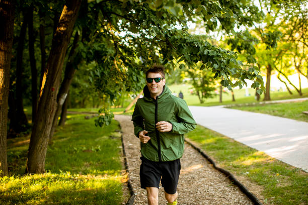 Handsome athletic young man running while doing workout in sunny green park