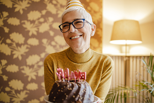 A mature woman is holding a birthday cake and smiling
