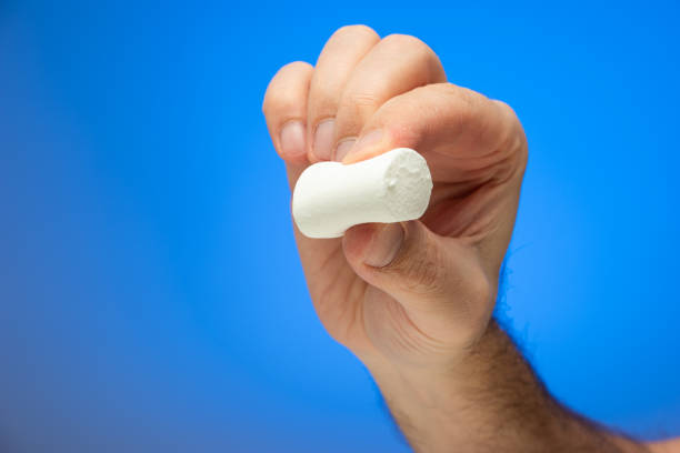 istock Single white marshmallow held between fingers by Caucasian male hand isolated against blue background studio shot close up 1301937275