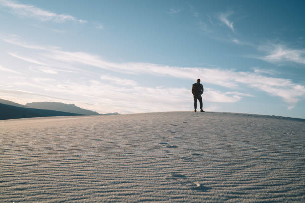 Back view of full body anonymous male traveler standing on empty sandy dune against cloudy blue sky in White Sands National Park