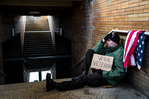Desperate homeless war veteran holding cardboard sign with text \