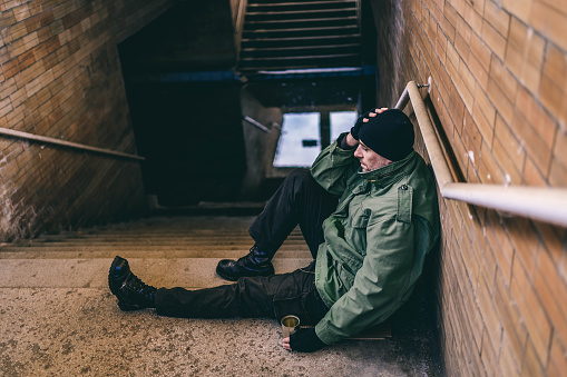 Young homeless depressed man sitting on subway station