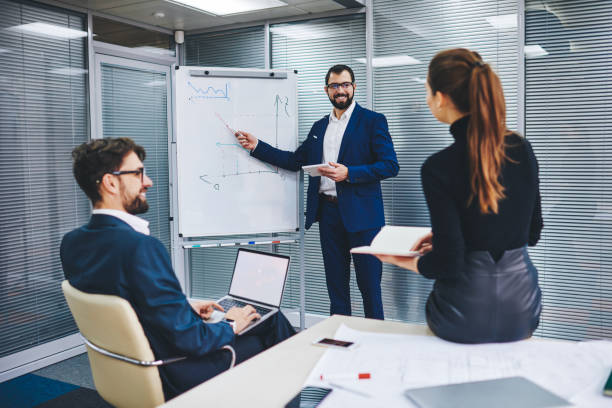 istock Male and female experts have coaching conversation for discuss statement for project checking infographics on flip chart, businessman communicating with office employees explaining revenue benchmark 1301943995