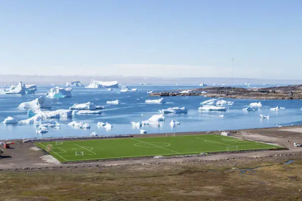 Qeqertarsuaq, Greenland - July 6, 2018: The local soccer field with icebergs in the background